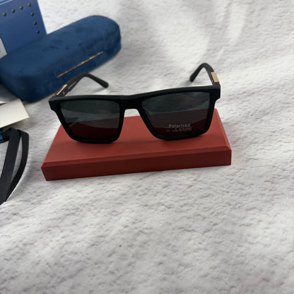 Matte black polarized sunglasses with gold logo detailing on temple arms, sitting on a red display b