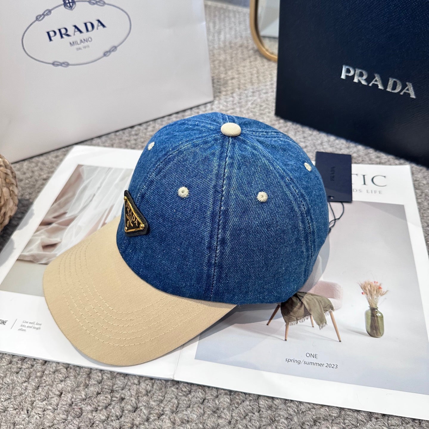 A two-tone baseball cap with a blue denim crown, beige brim, and a triangular metal logo badge.