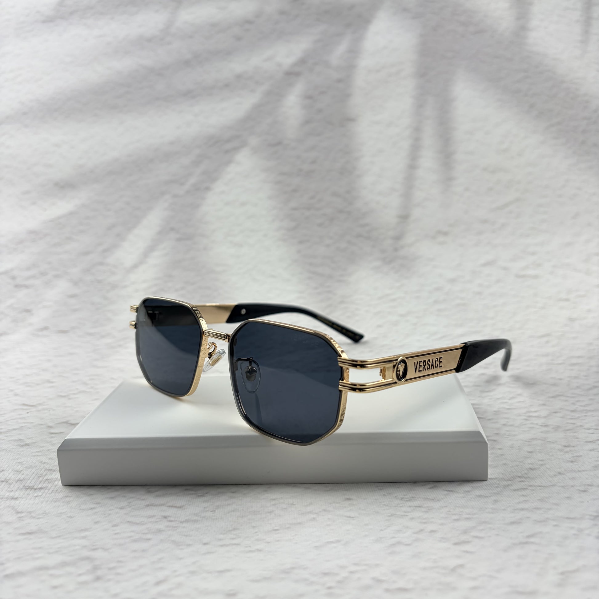 Gold tone metal frame geometric sunglasses with dark lenses on a white display block.