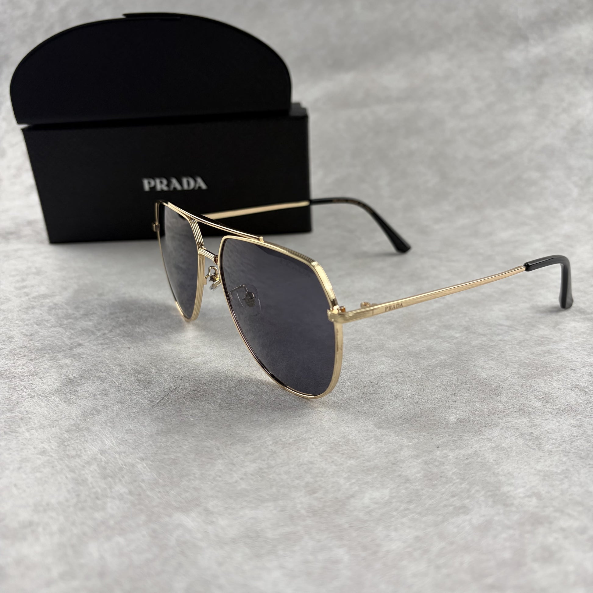 A pair of gold metal aviator sunglasses with dark lenses resting on a light grey textured background