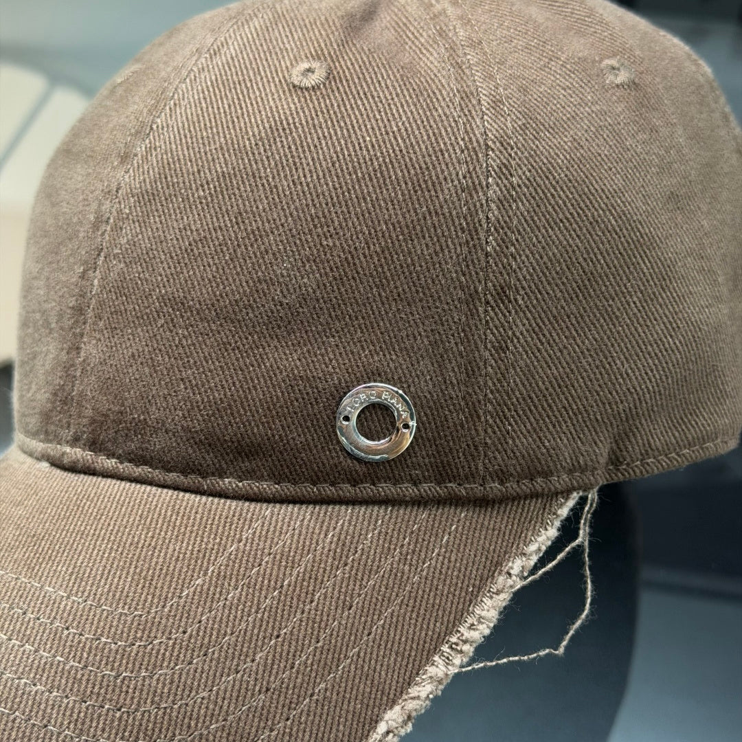 Distressed brown cotton baseball cap with frayed brim and minimalist metal circular side detail.