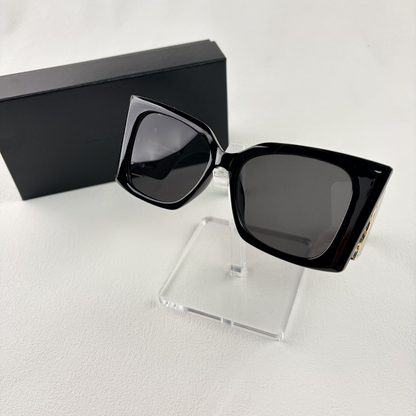 Pair of oversized black square sunglasses with gold metal logo accents on temples on display stand.