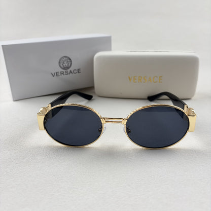 Oval gold metal frame sunglasses with black temples and dark tinted lenses, shown with a storage cas