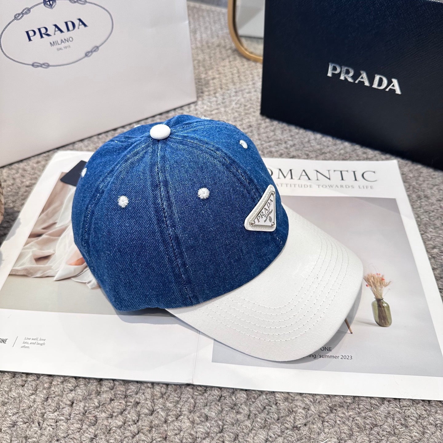 A stylish blue denim baseball cap with a white brim and a triangular metal-look logo patch.