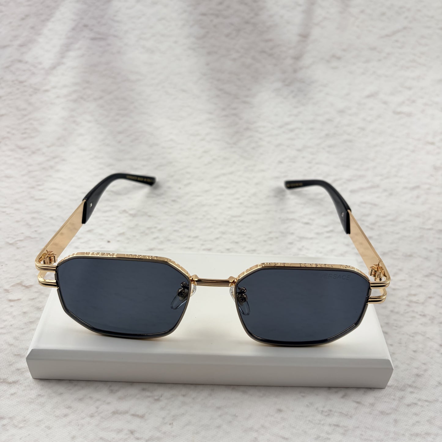 Gold tone metal frame geometric sunglasses with dark lenses on a white display block.