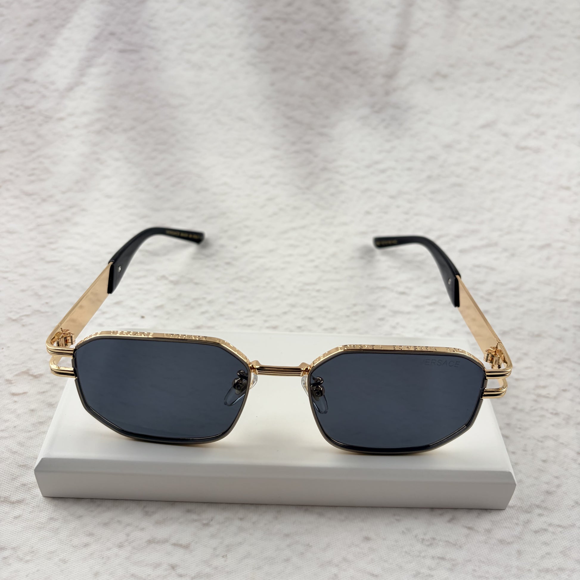 Gold tone metal frame geometric sunglasses with dark lenses on a white display block.