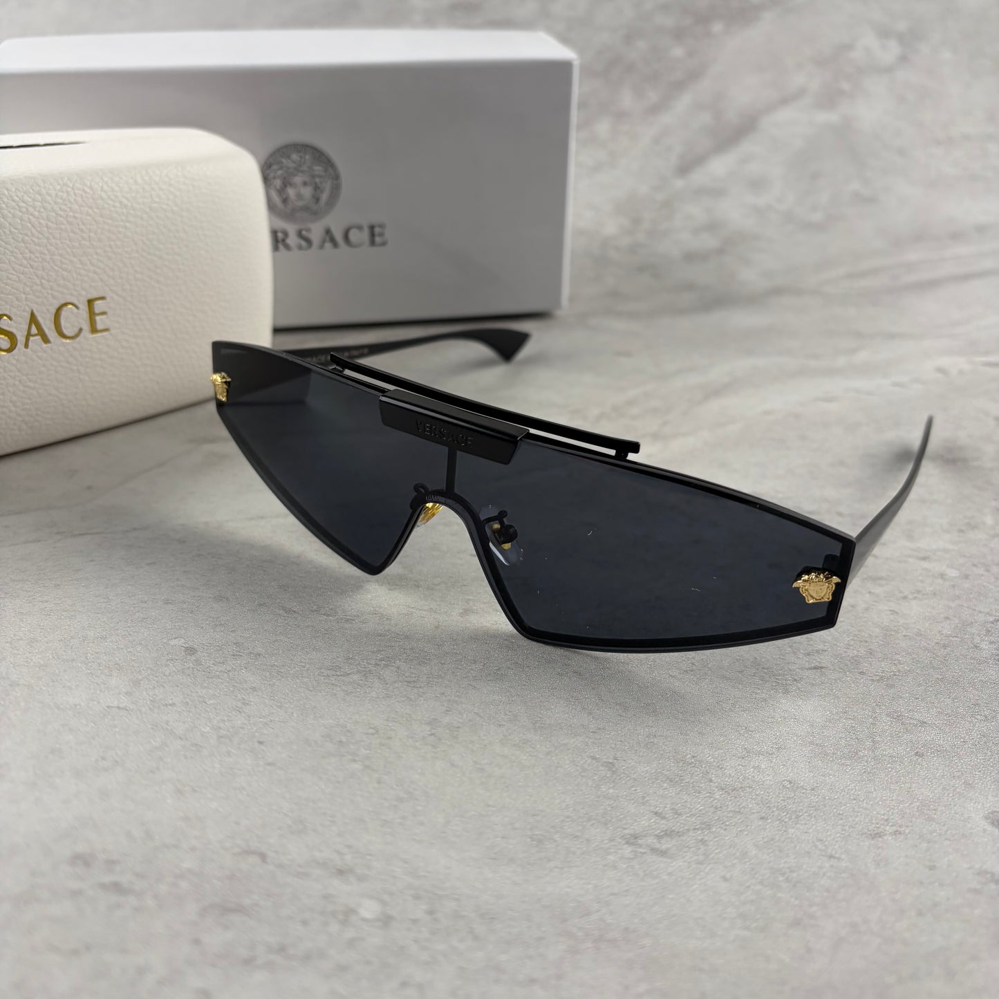 Modern shield sunglasses with a sleek black frame and dark tinted lenses on a grey background.