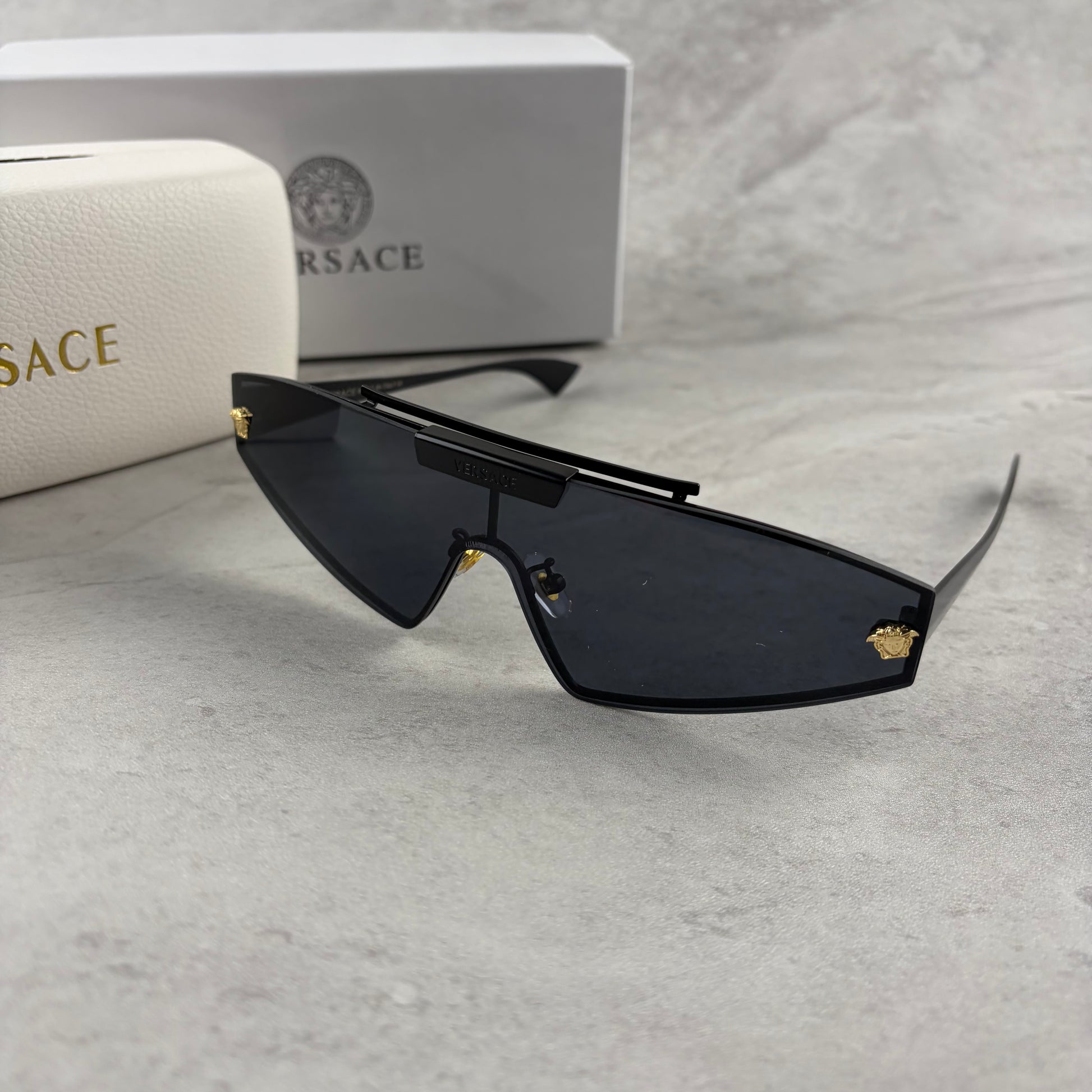 Modern shield sunglasses with a sleek black frame and dark tinted lenses on a grey background.