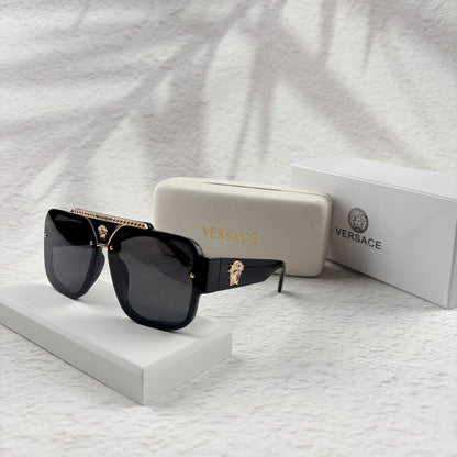 Oversized black flat-top sunglasses with a gold metal bridge and gold emblems on the temples.
