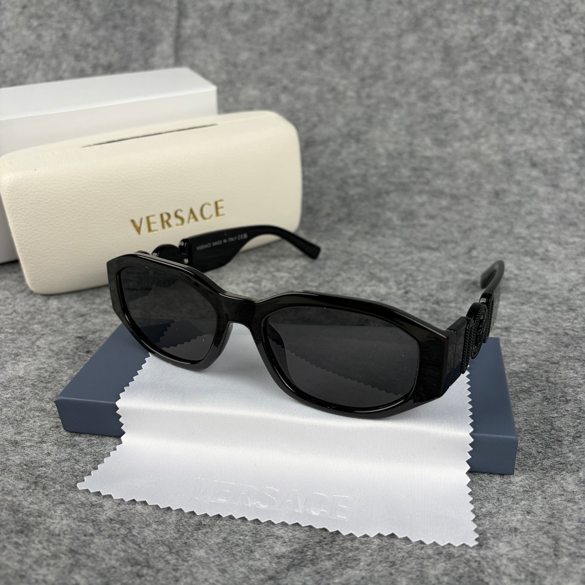 A pair of sleek black oval sunglasses resting on a cleaning cloth next to a white protective case.