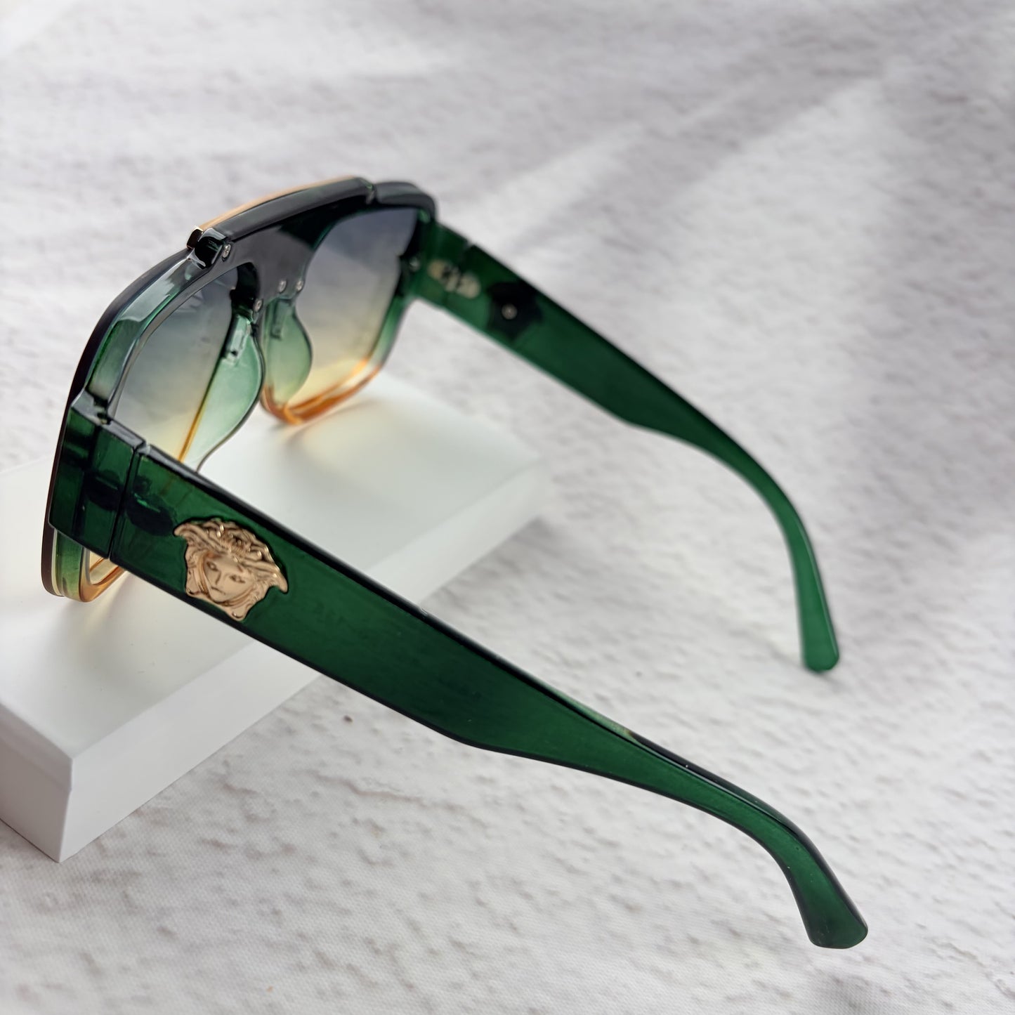 Oversized geometric sunglasses with green-to-yellow gradient lenses and gold metallic frame details.