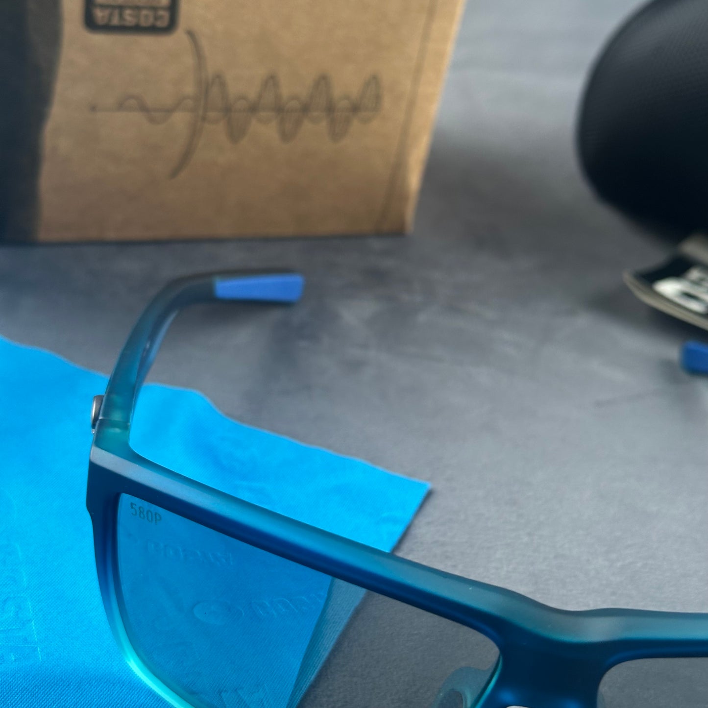 Blue and teal gradient frame sport sunglasses with polarized lenses resting on a blue cloth.